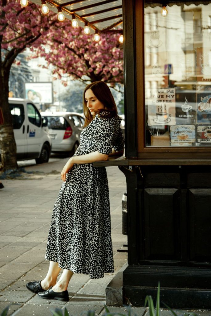 young brunette woman in patterned midi dress leaning on a kiosk
