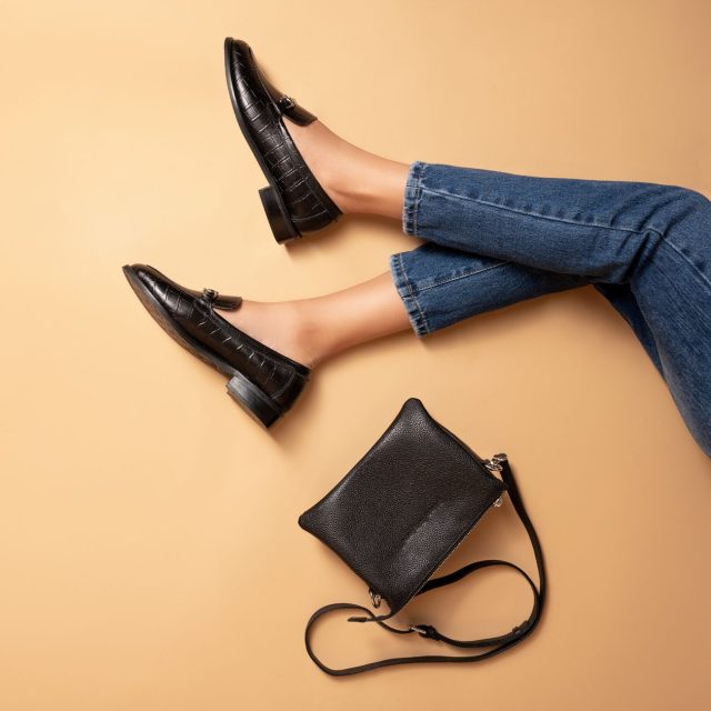 woman posing lying wearing black crocodile skin loafers and black purse