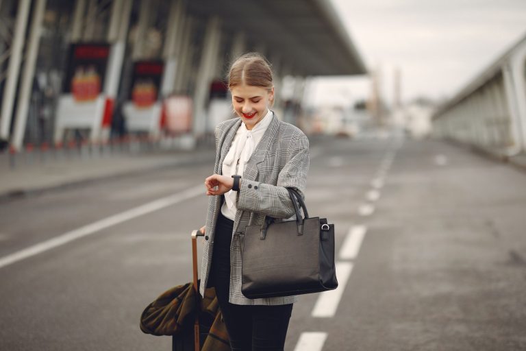 positive young businesswoman with suitcase hurrying on flight on urban background