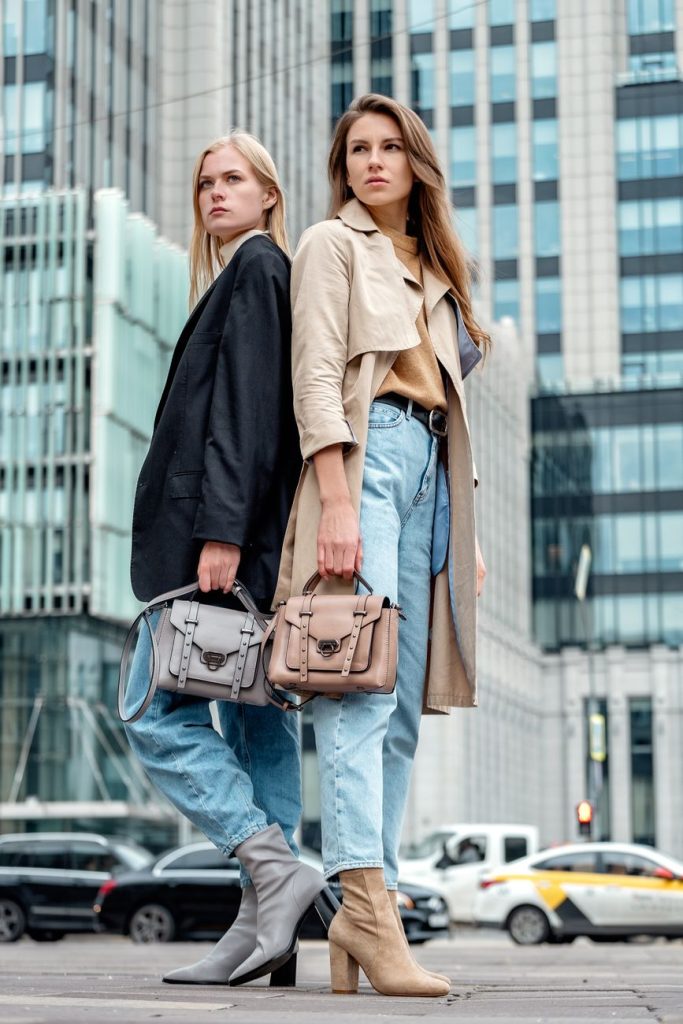women standing in the middle of the city area wearing coasts and holding a handbag
